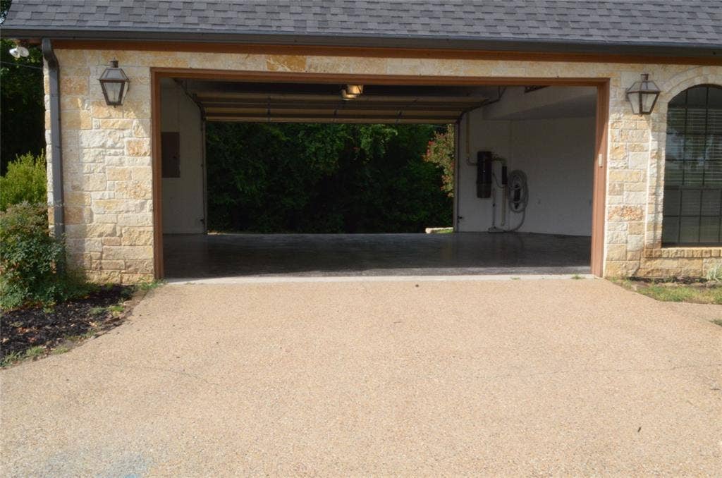 6414 Dorsey Drive, Athens, TX 75752 Exposed aggregate driveway leading to a two-car garage with stone veneer exterior, architectural shingle roof, and carriage-style outdoor lighting fixtures