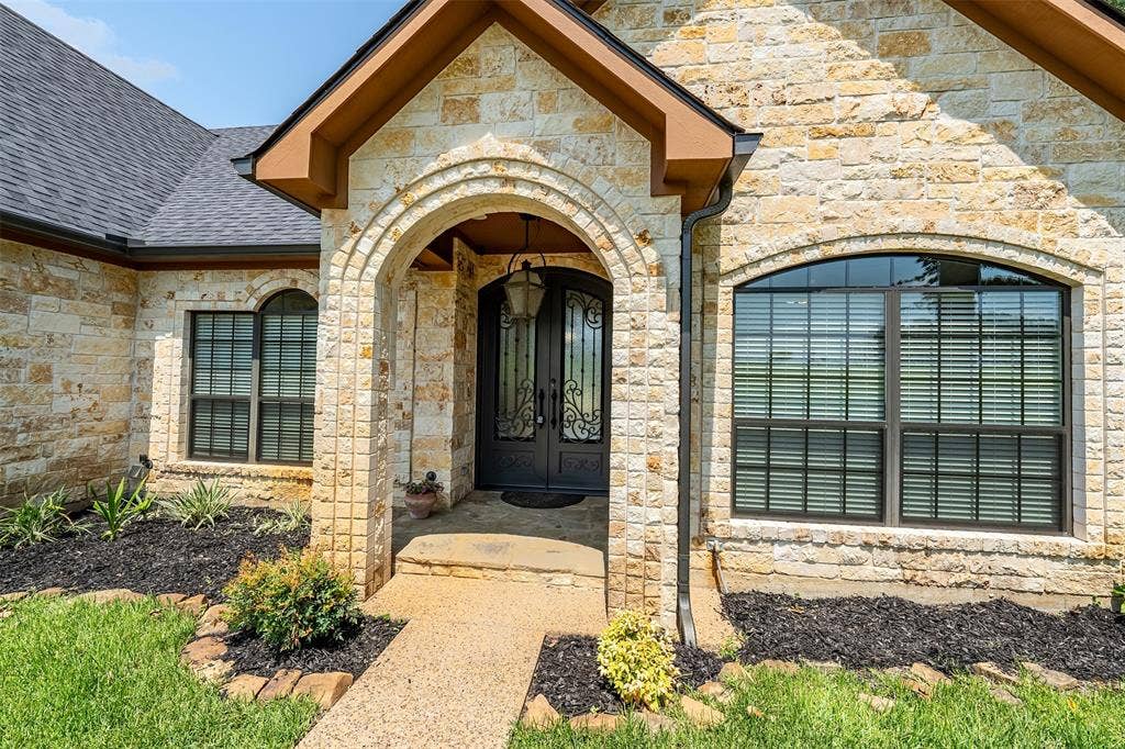 6414 Dorsey Drive, Athens, TX 75752 Stone facade entry featuring an arched doorway with iron double doors, an overhead pendant light fixture, and arched windows with horizontal blinds