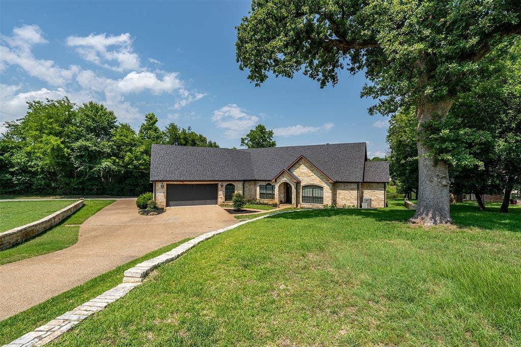 6414 Dorsey Drive, Athens, TX 75752 Stone-clad residence featuring a dark shingle roof, arched entryway, and a two-car garage