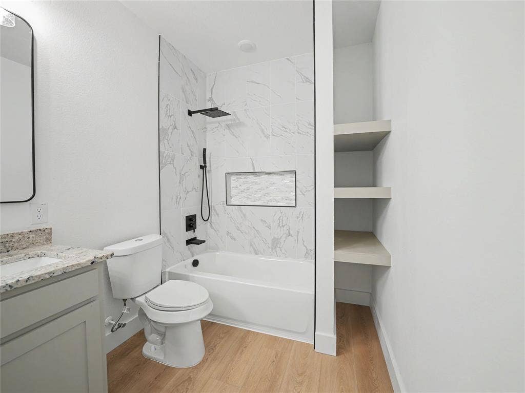 113 Dennis Drive, Azle, TX 76020 Contemporary bathroom featuring a white tub with marble-patterned tile surround, matte black shower fixtures, a built-in shower niche, and light wood-finish flooring