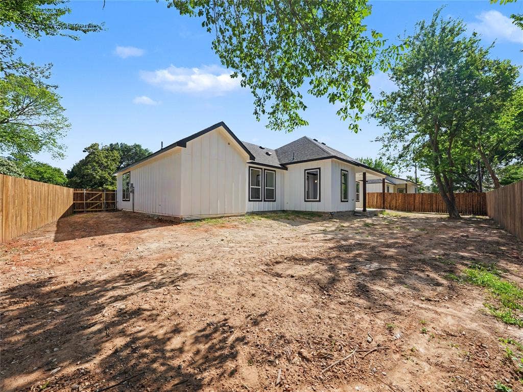 113 Dennis Drive, Azle, TX 76020 Spacious backyard featuring a newly installed wooden privacy fence, a covered patio area, and a white board-and-batten exterior with contrasting dark trim windows
