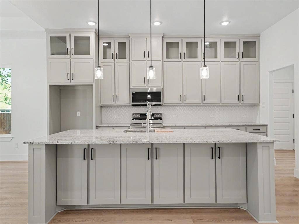 113 Dennis Drive, Azle, TX 76020 Central kitchen island with a light-toned countertop, shaker-style cabinetry, a built-in sink, and three pendant light fixtures