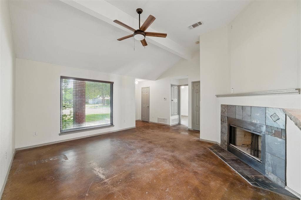 Unfurnished living room with concrete floors, a tiled fireplace, a ceiling fan, beamed ceiling, and high vaulted ceiling