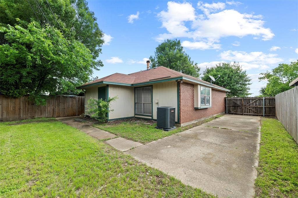 Back of property featuring cooling unit, concrete driveway, a gate, and brick siding