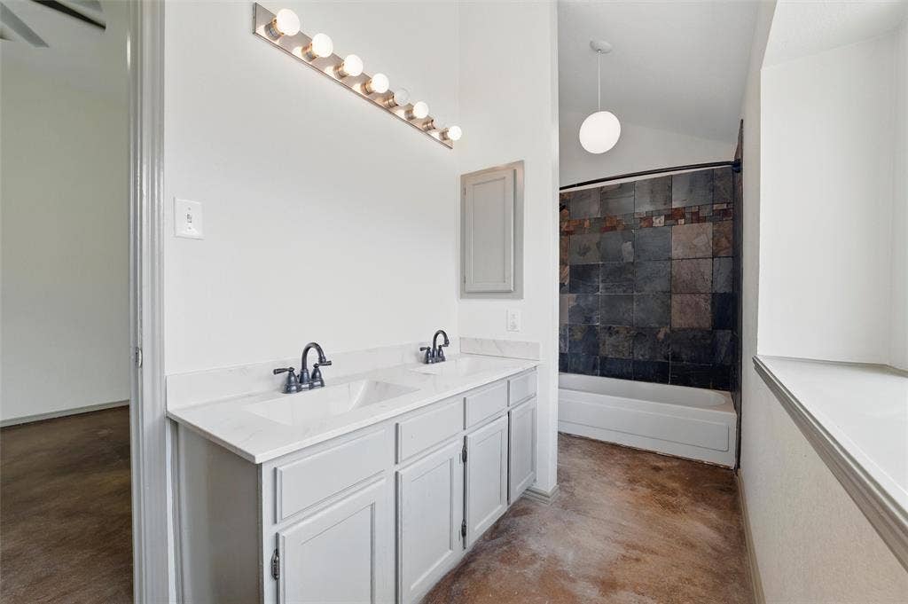 Bathroom with concrete floors, double vanity, lofted ceiling, and shower / washtub combination