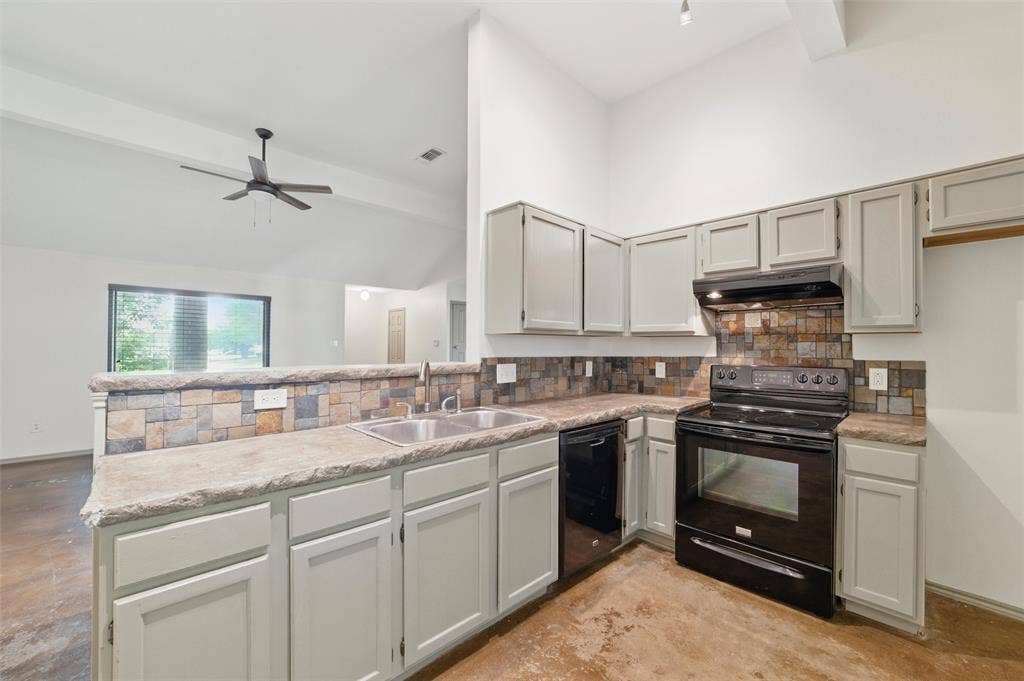 Kitchen featuring black appliances, a sink, a peninsula, under cabinet range hood, and concrete floors