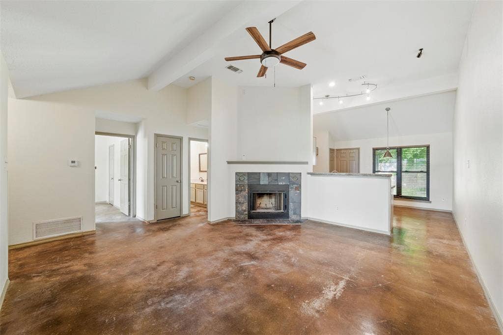 Unfurnished living room with a ceiling fan, concrete flooring, beamed ceiling, a tiled fireplace, and baseboards