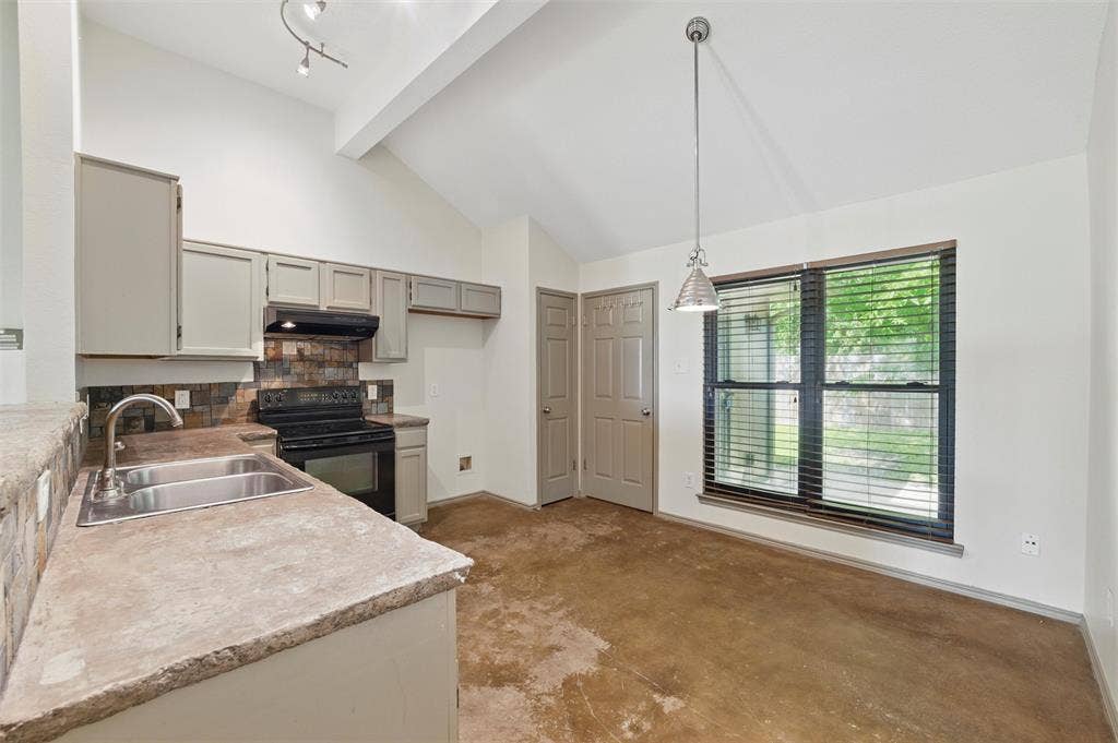 Kitchen featuring black range with electric stovetop, a sink, under cabinet range hood, concrete floors, and light countertops