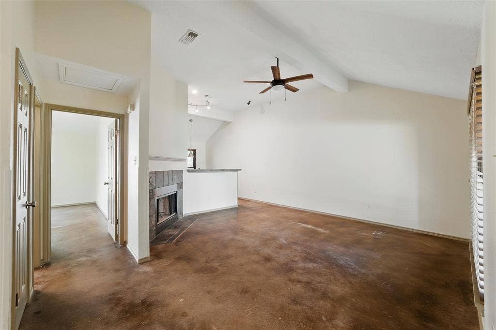 Unfurnished living room with ceiling fan, concrete flooring, and a tiled fireplace
