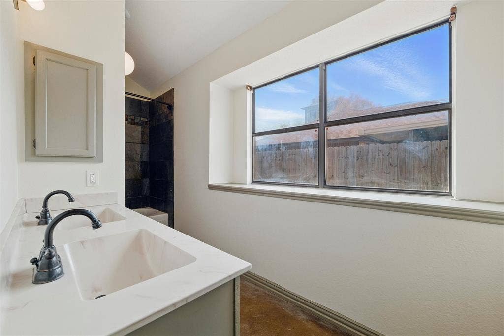 Bathroom with vanity, vaulted ceiling, concrete flooring, and a shower