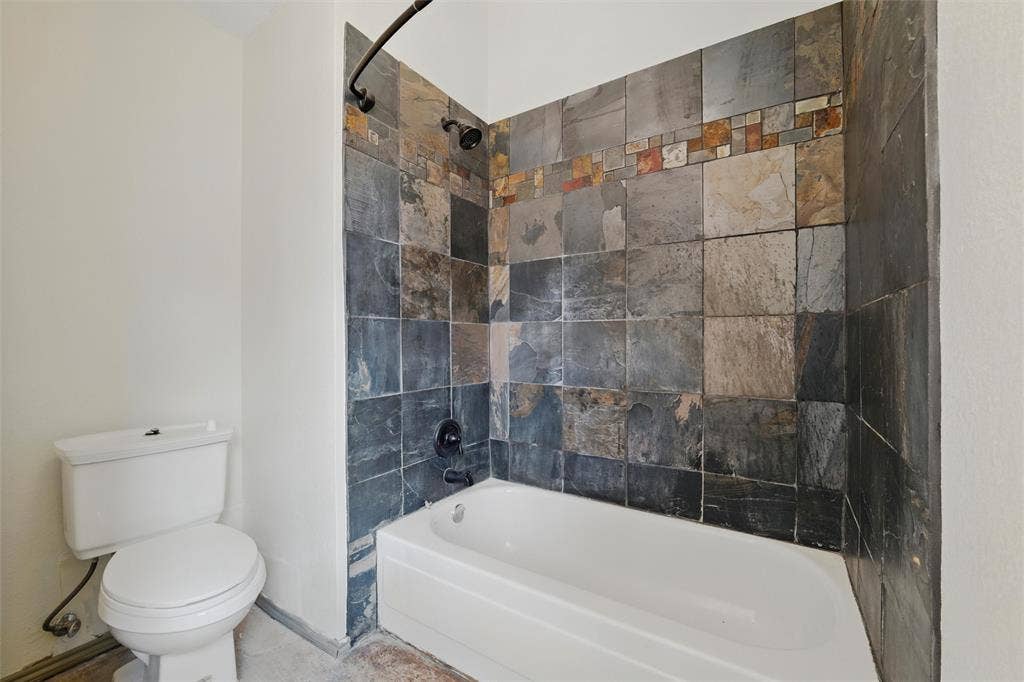 Full bath featuring toilet, washtub / shower combination, and baseboards
