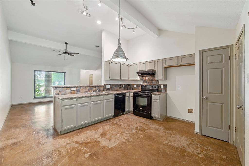 Kitchen featuring black appliances, under cabinet range hood, a sink, concrete floors, and a peninsula