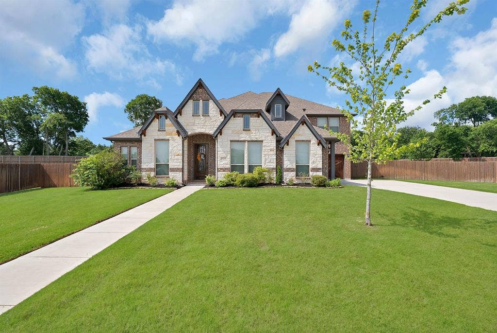 Two-story residential exterior featuring a stone and brick facade, gabled rooflines, and dormer windows