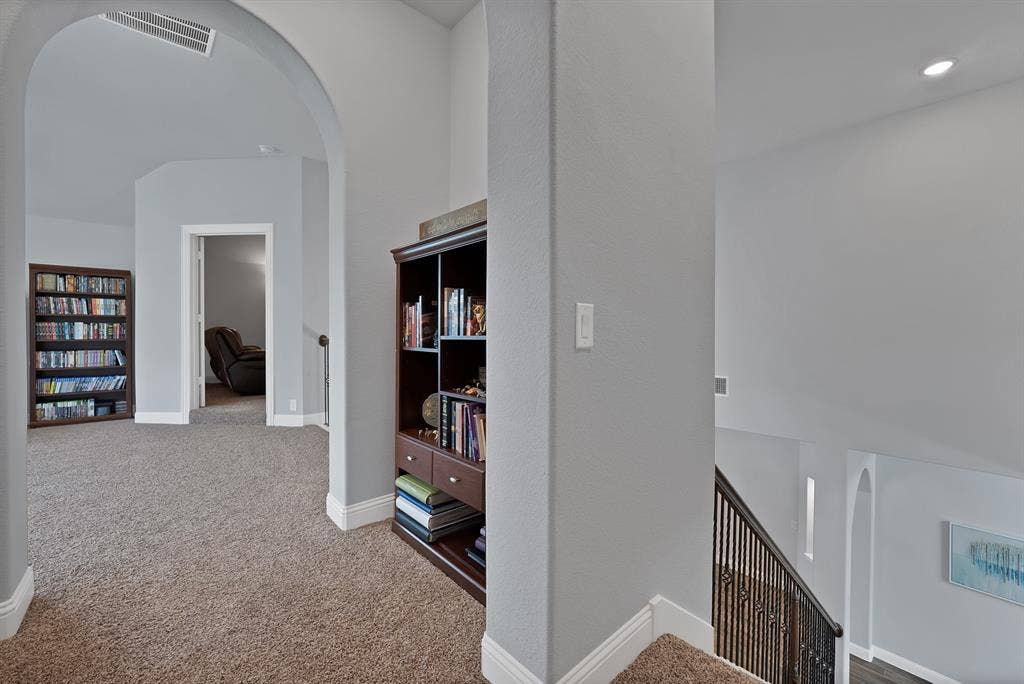 Upper-level hallway featuring arched doorways, light gray wall paint, and plush carpeting