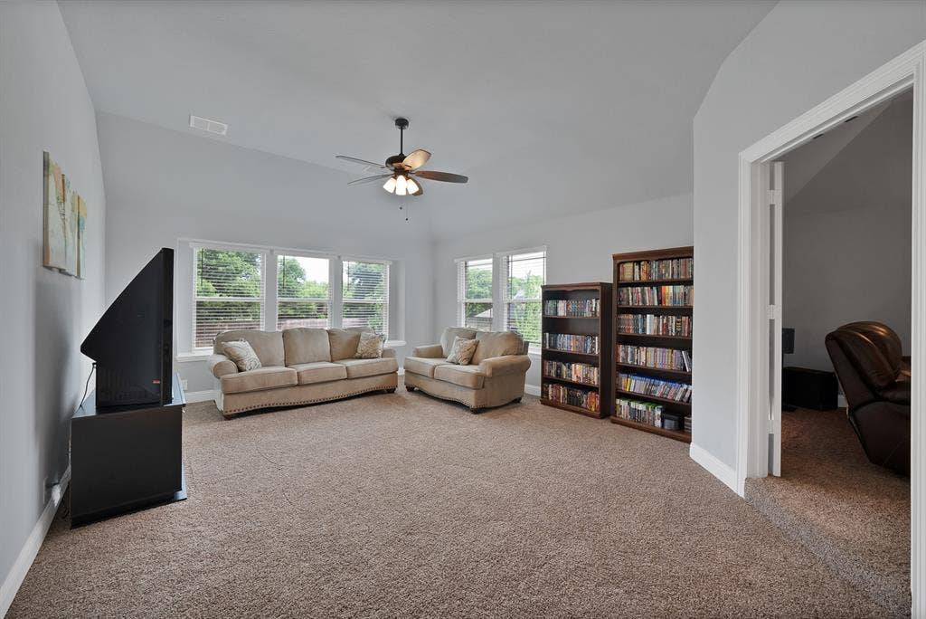 Carpeted entertainment room featuring vaulted ceilings, multiple windows with blinds, and an overhead ceiling fan with lighting