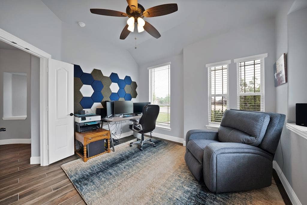 Room featuring wood-finish flooring, vaulted ceiling, and multiple windows with blinds