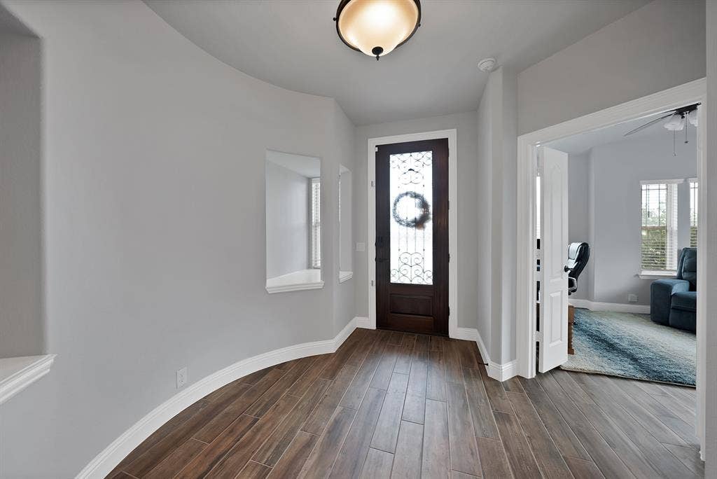 Entryway featuring wood-finish flooring, a dark wood front door with decorative glass, and a curved wall with display niches
