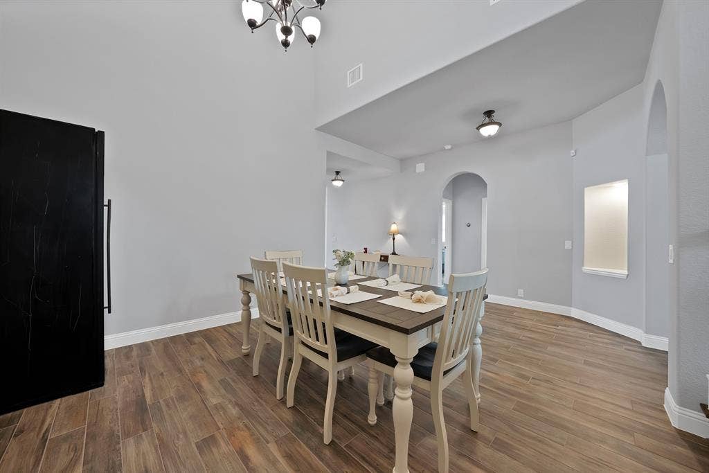 Spacious dining area featuring wood-finish flooring, vaulted ceilings, arched doorways, a built-in wall niche, and a contemporary chandelier