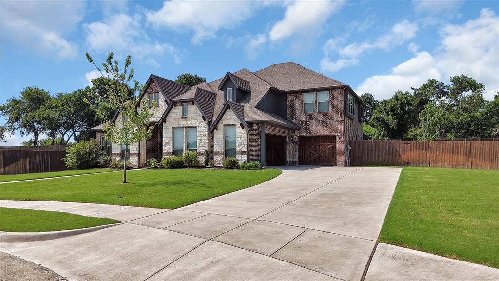 Two-story residence featuring a brick and stone facade, a multi-gabled roofline, and a concrete driveway