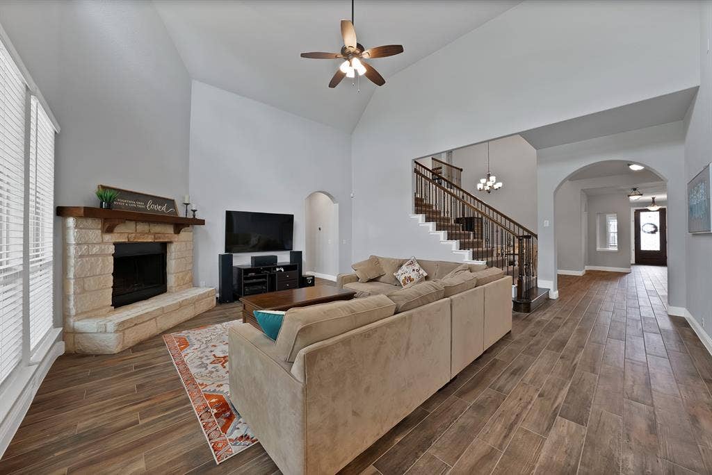 Spacious living area featuring high vaulted ceilings, wood-finish flooring, and a stone fireplace with a substantial wood mantle