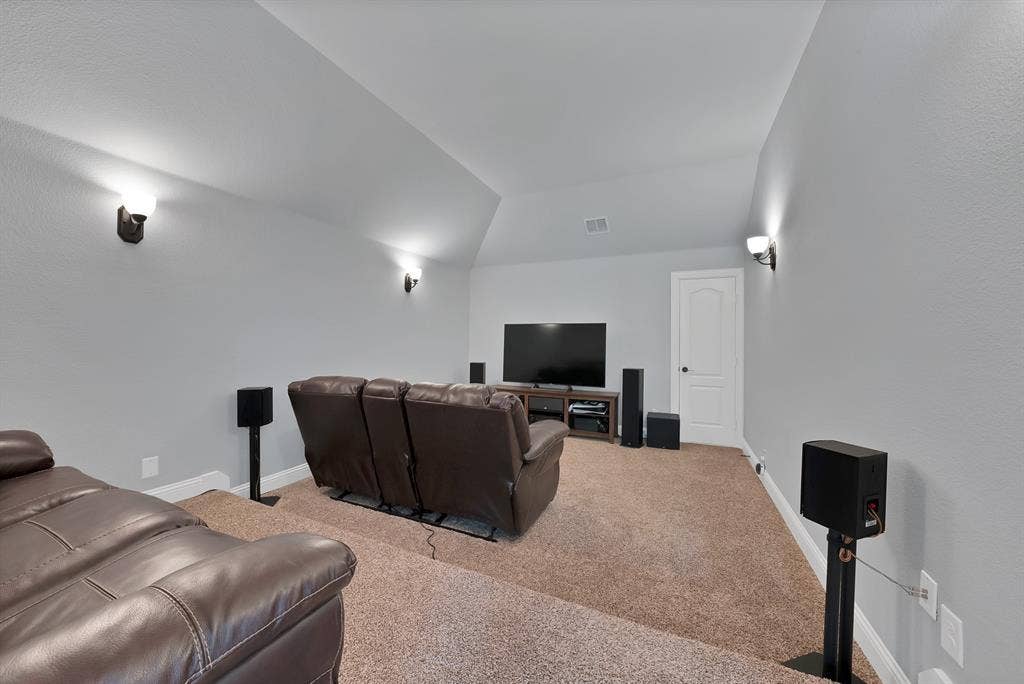 Carpeted media room featuring sloped ceilings, wall sconces, a built-in media console, and a paneled interior door