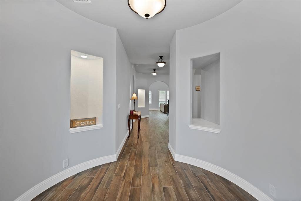 Hallway featuring wood-finish flooring, light gray walls, coved baseboards, recessed display niches, and ceiling-mounted light fixtures