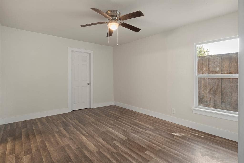 Bright interior room featuring wood-finish flooring, a ceiling fan with integrated lighting, and a white paneled door