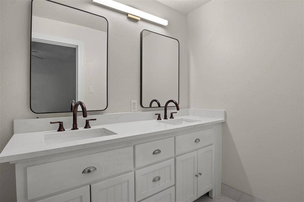 Double vanity featuring white cabinetry, integrated sinks, white countertops, and oil-rubbed bronze hardware