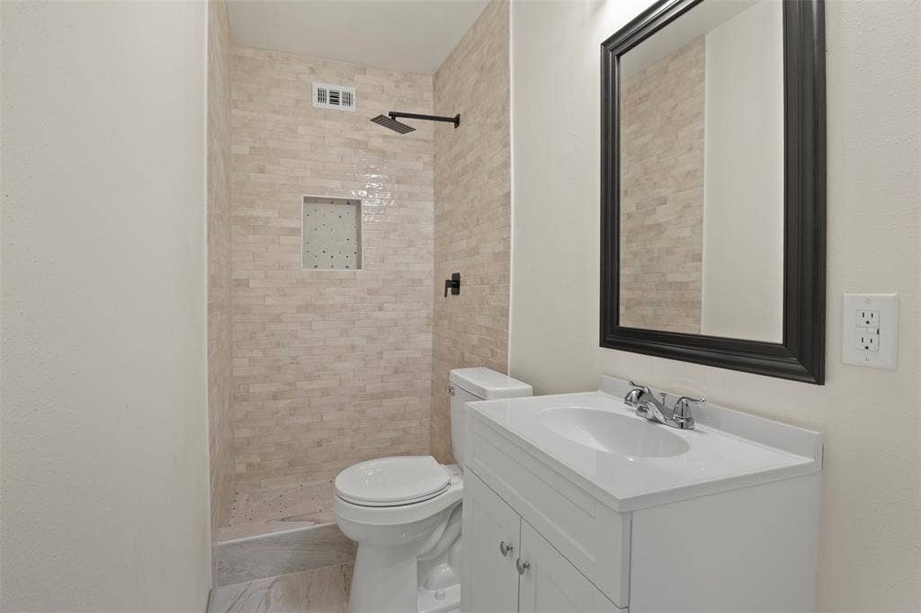 ensuite Bathroom in large bedroom upstairs featuring a shower with light-toned rectangular tile, a built-in shower niche, and a matte black rainfall showerhead