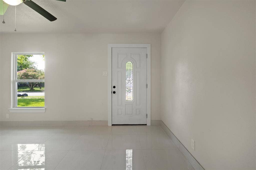 Entryway featuring a white door with decorative glass inserts, a single-pane window, light-colored walls, and glossy tile flooring