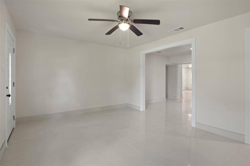 Expansive living area featuring light-toned tile flooring, neutral wall paint, and a ceiling fan with integrated lighting