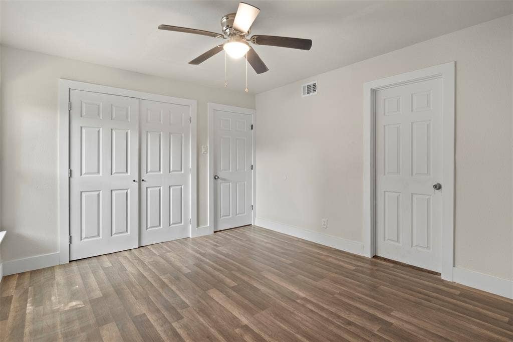 Bright room featuring wood-finish flooring, a ceiling fan with integrated lighting, and white baseboards