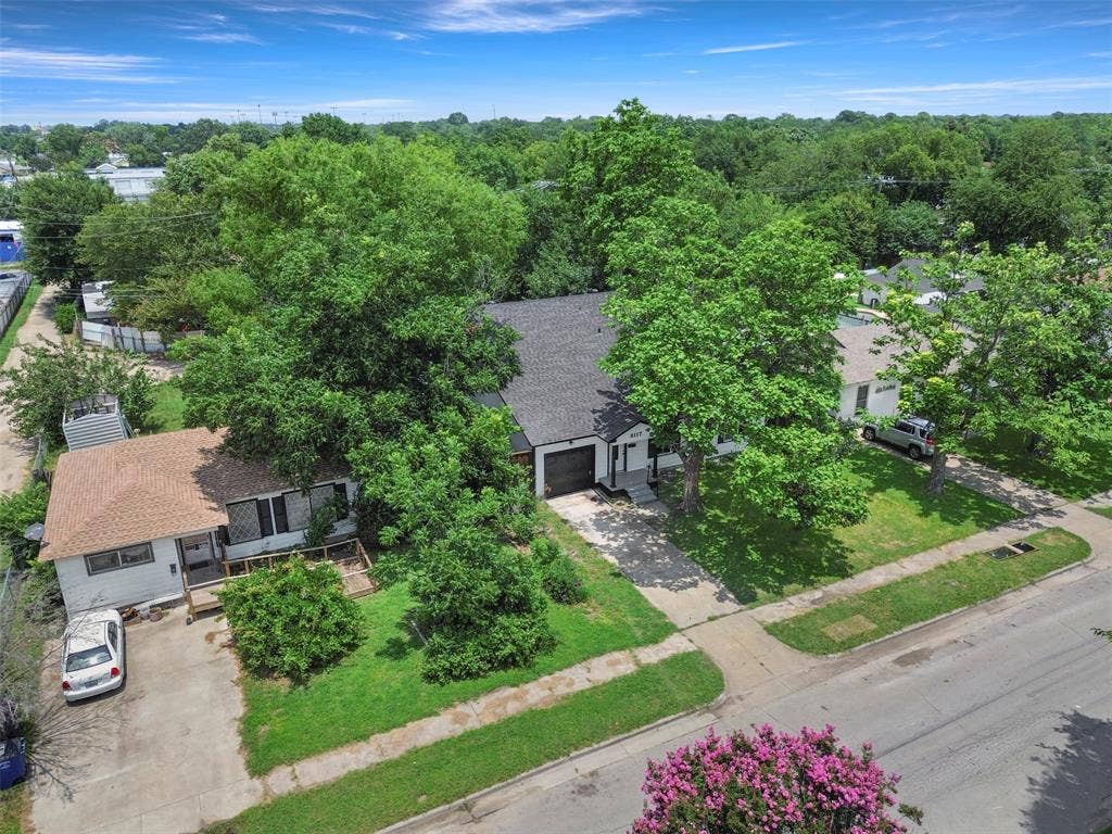 Residential property featuring a dark shingle roof, mature trees, and a concrete driveway