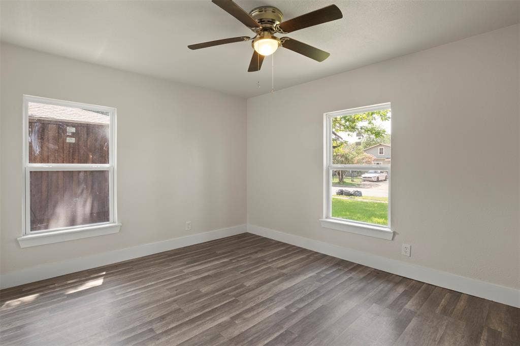Open room featuring wood-finish flooring, two windows with white trim, and a ceiling fan with integrated lighting