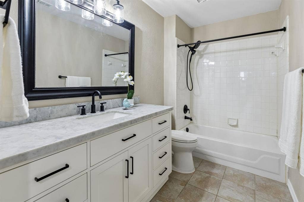 607 Grimsworth Court, Allen, TX 75002 Updated guest bath offers quartz countertop,framed mirror, fresh paint, white cabinetry with black fixtures and tub with shower.