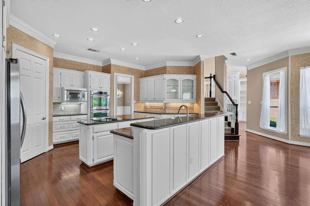 Kitchen featuring two islands with stone countertops, white cabinetry, integrated double ovens, and wood-finish flooring