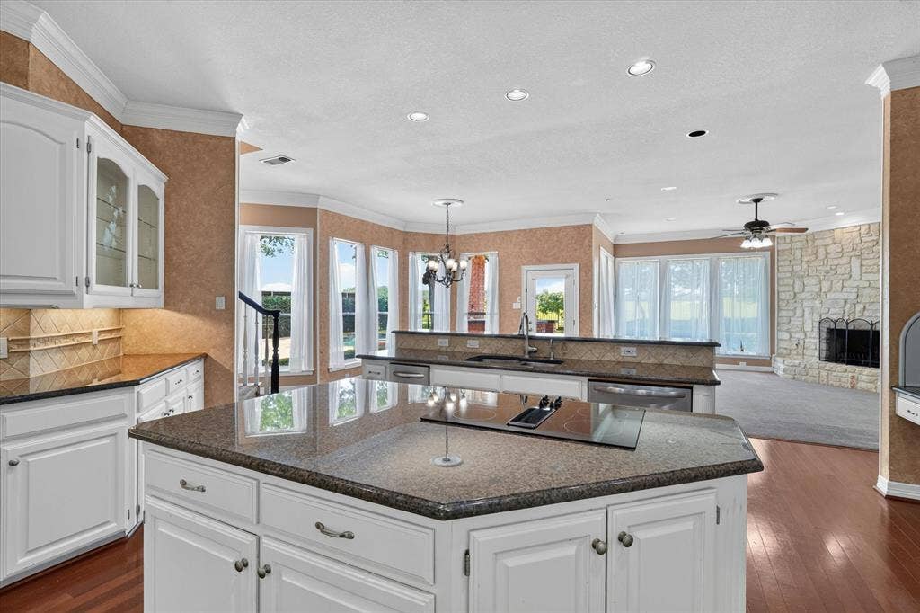 Expansive kitchen featuring a large central island with an integrated cooktop, white cabinetry, and granite countertops