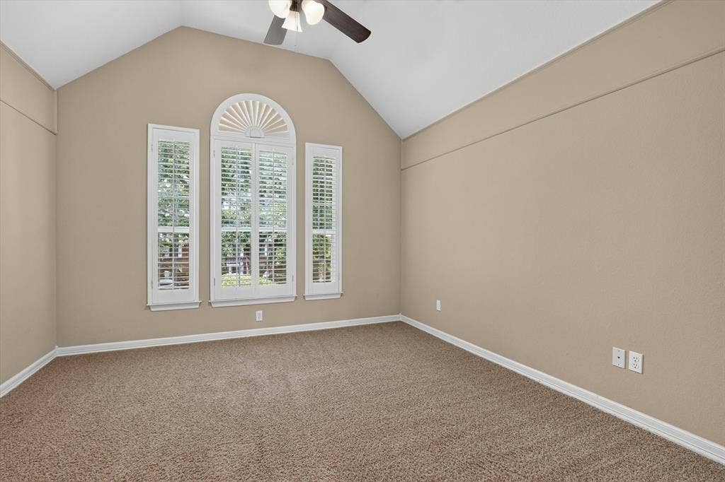 Vaulted ceiling with a ceiling fan, arched window with plantation shutters, two rectangular windows with plantation shutters, neutral wall color, and wall-to-wall carpet flooring