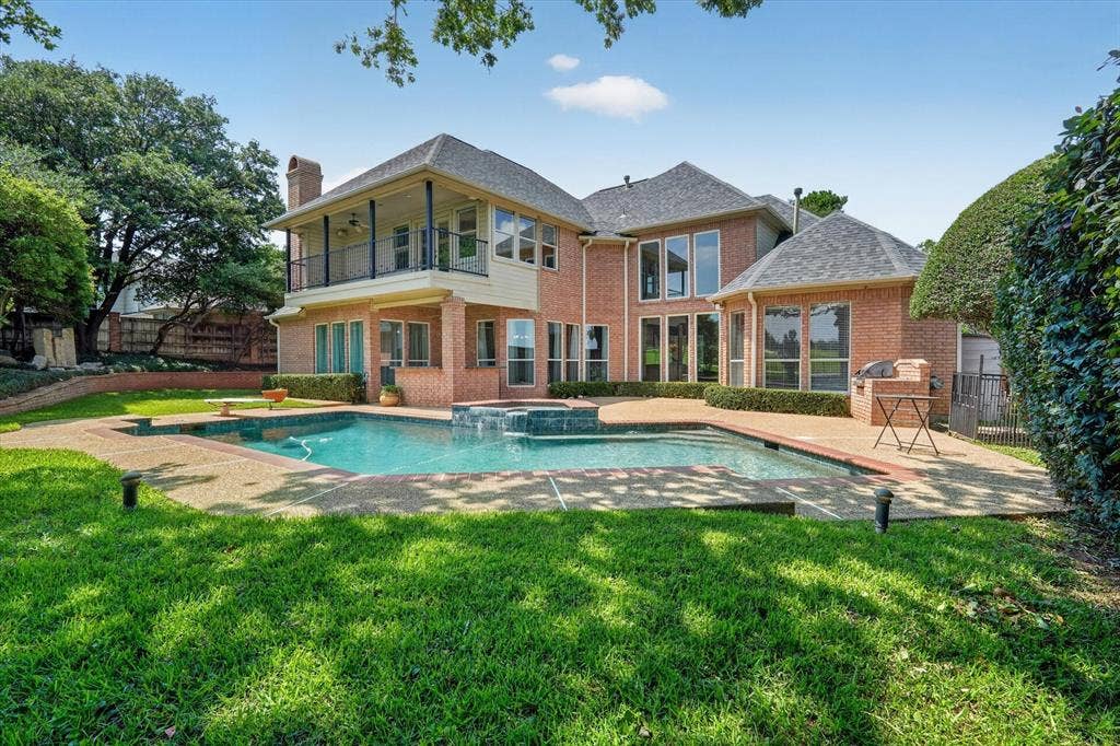 Brick exterior residence featuring a rear patio with a built-in pool and spa