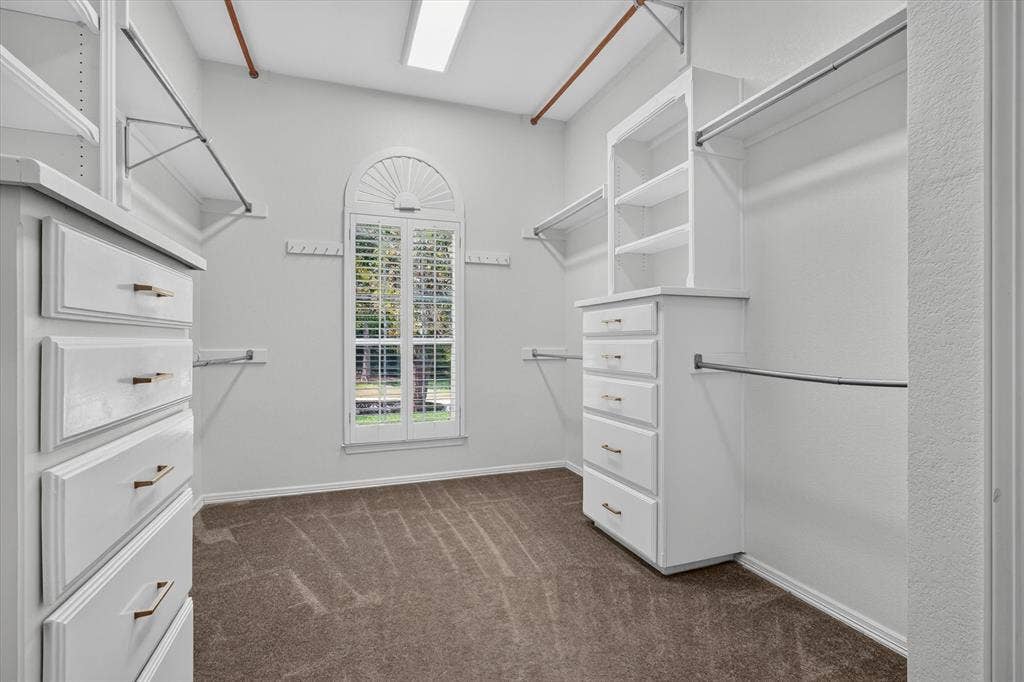 Walk-in closet featuring built-in cabinetry, integrated shelving, hanging rods, an arched window with plantation shutters, and carpet flooring