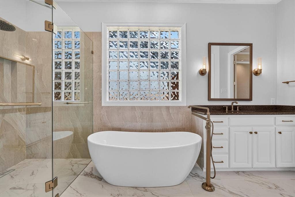 Freestanding soaking tub with a floor-mounted bronze-finish faucet, set against a backdrop of glass block windows