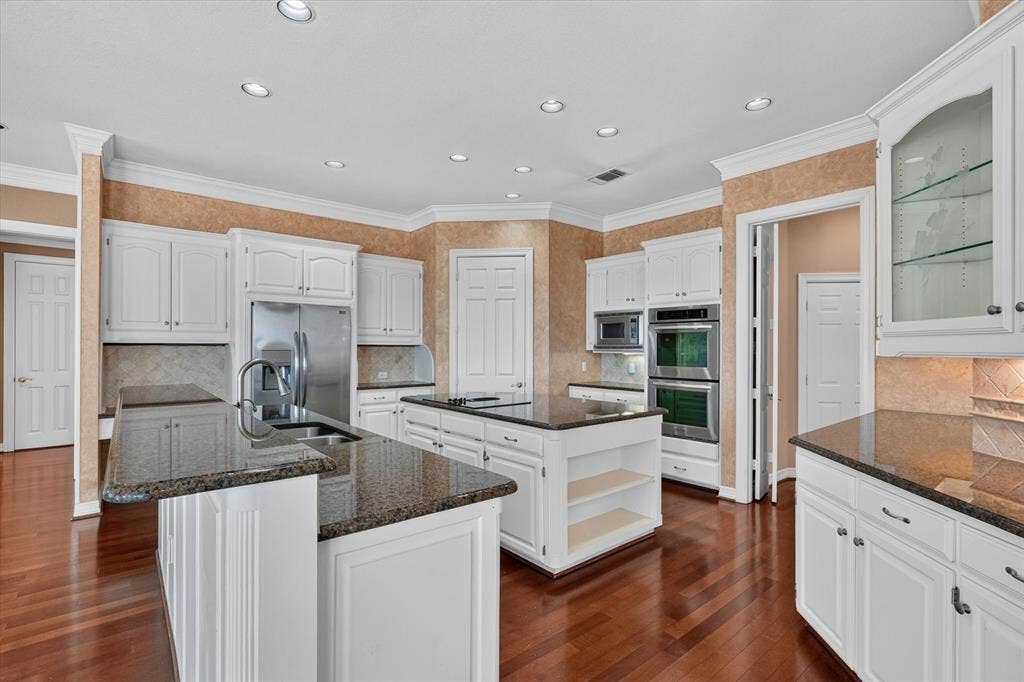 Kitchen featuring wood-finish flooring, white cabinetry, dark stone countertops, stainless steel appliances, and an island with built-in shelving