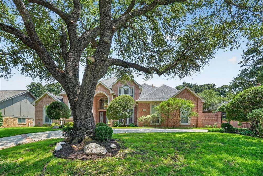 Brick exterior residence featuring a prominent mature tree, arched entryway, bay windows, and a multi-level roofline