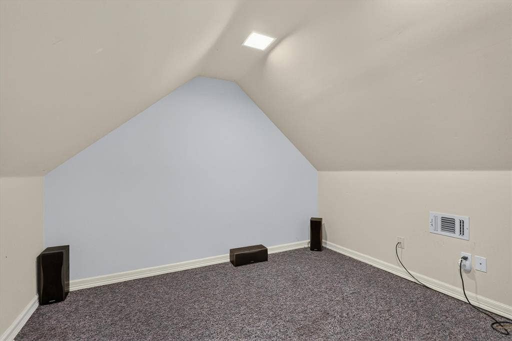 Sloped ceiling room featuring an attic ventilation grate and a recessed ceiling light