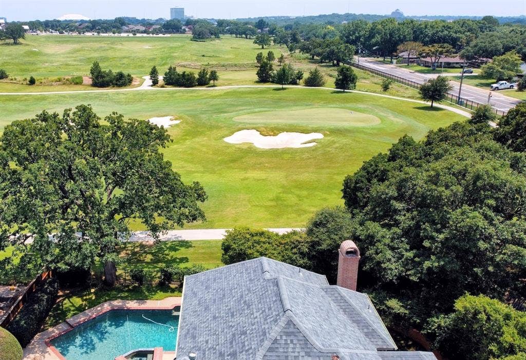 Aerial perspective showcasing a shingle roof with a brick chimney, overlooking a green golf course with sand traps