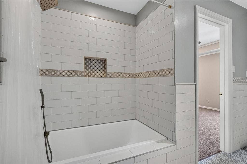 Built-in bathtub with subway tile surround, accent tile band, recessed shower niche, rain shower head, and handheld shower wand