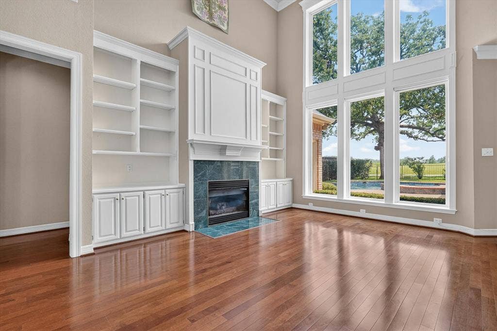 Two-story living room featuring a fireplace with a blue-green tile surround, built-in shelving, hardwood flooring, and tall windows