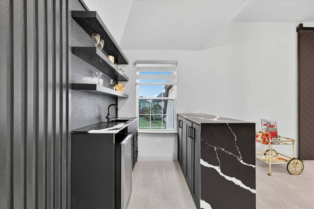 Contemporary wet bar featuring a black countertop with white veining, integrated sink, matte black faucet, and under-counter beverage refrigerator