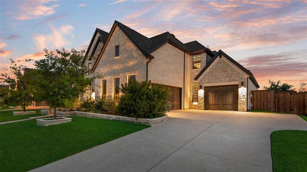 Stucco and stone exterior featuring multiple gables, a dark shingle roof, and a privacy fence