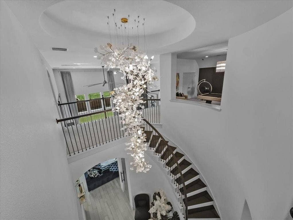 Grand entryway featuring a multi-tiered chandelier, curved staircase with dark wood treads and wrought iron balusters, and a second-story overlook with a half-wall cut-out